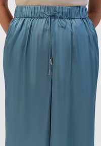 Light blue, satin, wide-leg pants with an elastic waistband and drawstring. Features shiny metallic aglets at the end of the drawstring.