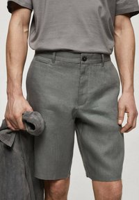 Shorts en lin gris avec une fermeture à bouton et des poches latérales, associés à une chemise grise à manches courtes. Le tissu a une texture lisse.