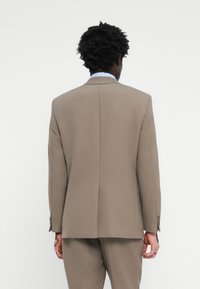 Brown suit jacket with a structured design, single vent at the back, and buttoned sleeves. Tailored fit and smooth texture.