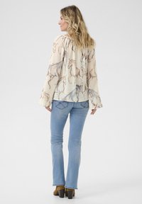 Blusa leggera color crema con motivo a cavallo, maniche lunghe a campana, abbinata a jeans svasati blu chiaro e stivaletti con tacco marroni.