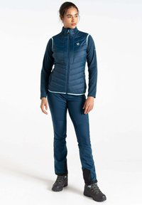 Marineblauer isolierter Weste mit gestepptem Muster und hohem Kragen, kombiniert mit passenden schmalen Hosen, die schwarze Akzente aufweisen, sowie robustem Schuhwerk.