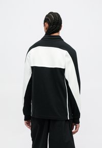 Svart og hvit jakke med en kontrasterende hvit panel over den øvre ryggen, med en avslappet passform og teksturert stoff.