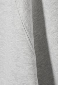 Sudadera gris claro fabricada en un tejido suave, con una superficie texturizada que presenta un detalle de costura visible y una variación de color discreta.