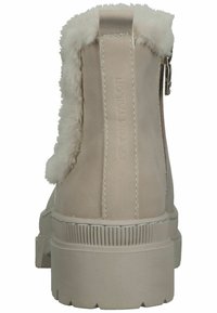 Bottes chelsea beiges avec doublure en fausse fourrure, texture en daim lisse, fermeture éclair et semelle en caoutchouc robuste avec accents nervurés.
