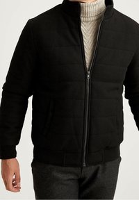 Svart quiltad jacka med hög krage, dragkedja fram och sidofickor, tillverkad av texturerat tyg. Anmärkningsvärda ribbade mudd och midja.