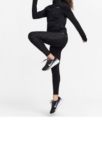 Svart zip-up sportjacka och leggings med glittrande mönster, tillsammans med svarta och vita löparskor med en swoosh-logotyp.