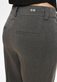 Graue, maßgeschneiderte Hosen zeichnen sich durch eine glatte Textur, eine taillierte Silhouette und Gesäßtaschen aus. Der Bund ist mit zwei dekorativen grauen Punkten versehen.