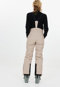 Beige skibroek met zwarte accenten aan de zijkant, verstelbare banden en een getailleerde taille, gemaakt van duurzaam materiaal voor wintersport.