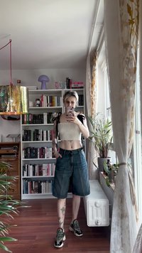 Top corto blanco con textura acanalada y tirantes negros, combinado con pantalones cortos de mezclilla azules holgados. Incluye zapatillas negras y verdes. Luz cálida interior.