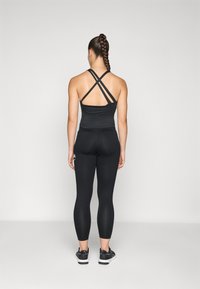 Svart treningssinglet med kryssbelagt rygg, sammen med svarte leggings og treningssko. Glatt stoff og tettsittende design.
