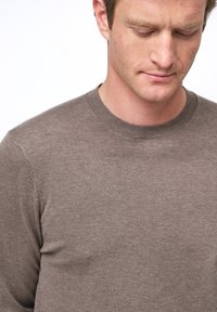 Maglione a collo rotondo marrone realizzato in morbido tessuto a maglia. Caratterizzato da una sottile texture e da un design aderente. Nessun motivo o decorazione visibile.