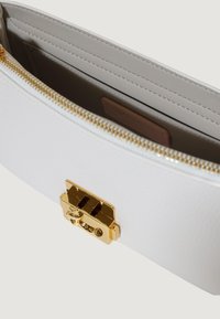 Bolsa de cuero blanca con cierre de metal dorado, cremallera y ranura interior para tarjetas. Textura suave y diseño minimalista.