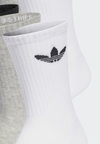 Drei Paar Socken in Weiß, Grau und Schwarz. Die weiße Socke zeigt ein schwarzes Adidas Trefoil-Logo und hat am oberen Rand eine gerippte Struktur.