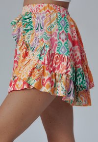 Multikleurige rok met ruffles, voorzien van een elastische tailleband, met een levendig patroon van roze, oranje, groen en paars in een lichtgewicht stof.