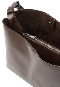 Brązowa torba typu tote wykonana z gładkiej skóry, z miękką podszewką wewnętrzną oraz kieszenią na zamek. Posiada regulowany pasek i zapięcie na zatrzask.