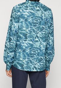 Camicia button-up con un motivo ad acqua blu, maniche lunghe e colletto classico. Tessuto liscio con una leggera lucentezza e vestibilità su misura.