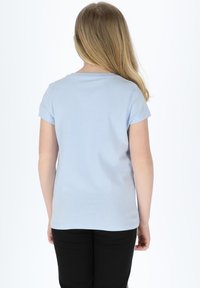 Light blue cotton t-shirt with short sleeves, round neckline, and a relaxed fit, paired with black pants, shown from the back.
