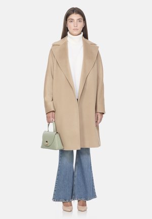 Cappotto lungo beige in lana con ampio colletto, abbinato a un dolcevita bianco, jeans a zampa d'elefante blu e una borsa verde menta. Scarpe del colore della pelle.