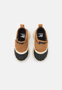 Bruna mockaskinn och svart texturerad tyg slip-on skor med vita gummisulor och kontrasterande accenter. Har en dragflik på baksidan.