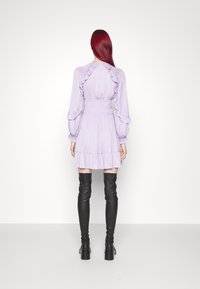 Lichtpaarse jurk met ruches, lange mouwen en een taille. Gecombineerd met zwarte overknee laarzen en een gladde textuur.