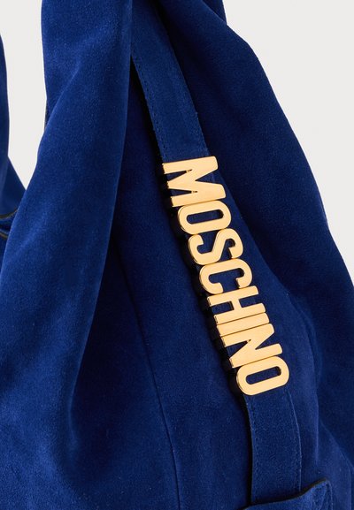 Tamno plava suđena torba s zlatnim akcentom "MOSCHINO" logotipa. Ima mekanu teksturu i ležeran dizajn, idealna za svakodnevnu ili casual upotrebu.