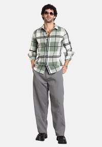Camicia a quadri verde e bianca con dettagli neri, pantaloni dritti grigi e scarpe platform nere. Gli accessori includono occhiali da sole.