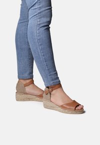 Bruna läder espadriller med öppen tå, klack av vävd jute och ankelrem, bärs tillsammans med blå skinny jeans.