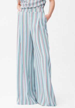 Jasnoniebieskie spodnie o szerokich nogawkach z pionowymi czerwonymi, białymi i niebieskimi paskami, noszone z rękami w kieszeniach na jednolitym białym tle.