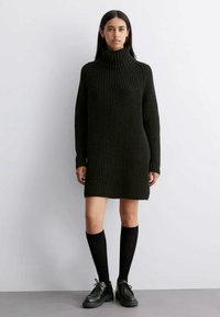 Μαύρο πλεκτό φόρεμα με ψηλό γιακά, με υφή, μακριά μανίκια και χαλαρή εφαρμογή, σε συνδυασμό με κάλτσες μέχρι το γόνατο και μαύρα παπούτσια.