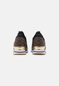 Black sneakers with a textured upper, gold accents on the heel, and a white and tan sole. Pattern features repeated logo design.