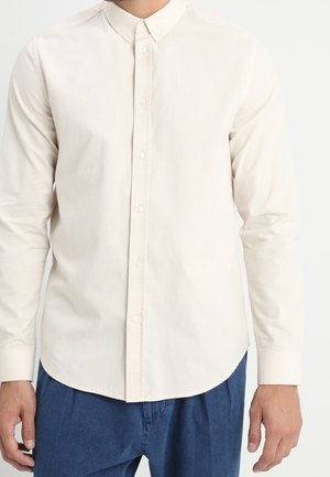 Chemise boutonnée beige clair avec des manches longues, un col pointu et un ourlet droit, fabriquée dans un tissu doux et lisse.