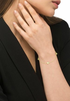 Goldenes Armband mit drei herzförmigen Anhängern an einer zarten Kette, die an einem Handgelenk vor einem schwarzen Kleidungsstück getragen wird.