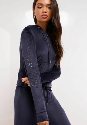 Mornarsko velur pulover s kapuco in zadrgo, z vrvico, dolgimi rokavi in besedilom okrašenim s kristali na levem rokavu.