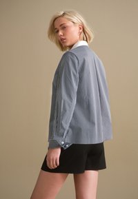 Blue and white striped long-sleeve shirt with a white collar, featuring buttoned cuffs and a relaxed fit, paired with black shorts.