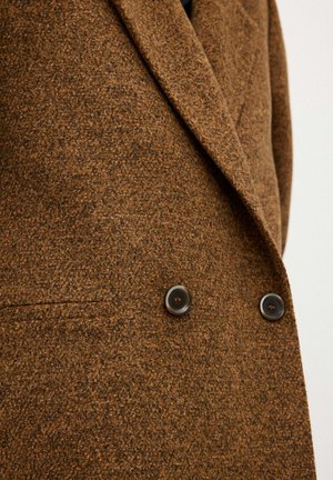 Brauner Wollblazer mit strukturiertem Material, doppelter Knopfleiste und zwei dunklen Knöpfen als bemerkenswerte Hardware-Details.