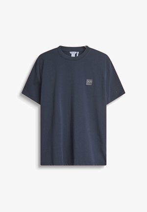 Camiseta de algodón de color azul marino con cuello redondo y mangas cortas. Presenta un pequeño parche con logo rectangular en el pecho. Diseño sencillo.