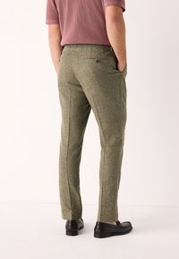 Olivengrønne teksturerede bukser med skræddersyet pasform, sidelommer og baglommer, kombineret med sorte loafers. Taljebåndet har bæltestropper.