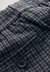 Geweven broek van donker marineblauw stof met een gestructureerd ruitpatroon, een opvallende zwarte knoop en subtiele stiksel details.