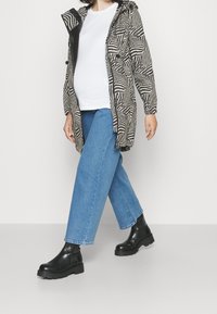 Giacca leggera a motivo zebra con cappuccio, dettagli neri e vita regolabile, abbinata a jeans in denim blu e stivaletti neri alla caviglia.