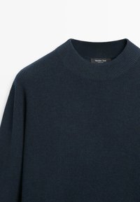 Granatowy dzianinowy sweter z szerokim, okrągłym dekoltem i prążkowaną fakturą, z metką z tyłu przy szyi.