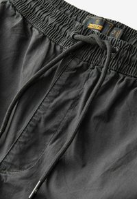 Costume de baie negre cu un elastic la talie, cordon ajustabil și textură netedă. Are un buzunar frontal și detalii de cusătură minime.