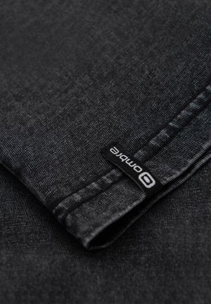 Zwarte denim stof met een gladde textuur, gevouwen rand en zichtbare stiksels. Een zwart label toont het woord "combit" in het wit.
