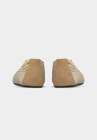 Paire de chaussures beige tissées à enfiler avec panneaux de talon en daim et semelles noires, vues de dos sur un fond blanc.