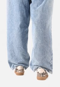 Pantaloni din denim de culoare albastru deschis, cu un croi lejer, purtați cu pantofi cu un design texturat în imprimeu de șarpe și o talpă de cauciuc maro.