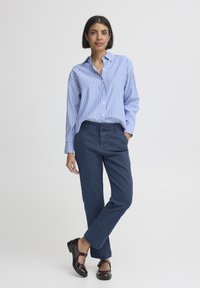 Világoskék-fehér csíkos gombos ing, sötétkék nadrág, fényes barna cipő, laza szabású, casual stílusban.