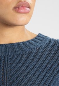 Suéter de punto azul oscuro con un cuello redondo acanalado y patrones de punto abierto con líneas verticales.