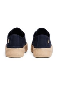 Kankurit-style kengät tummansinisen kanvaasin kanssa, luonnollisella juteepohjalla. Sisältää pienen logon kantapäässä ja sileän, tekstuurisen pinnan.