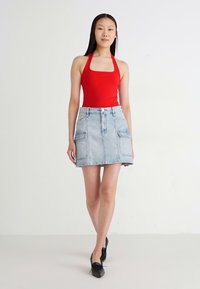 Rode haltertop gecombineerd met een lichtblauwe denim minirok met frontzakken, een rechte pasvorm en een knoopsluiting. Zwarte platte schoenen.