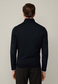 Marinblå tröja med långa ärmar, ribbade muddar och krage. Har mörka armbågsplåster och en slim fit-design. Mjuk, stickad textur.