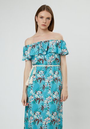 Maxi-jurk van turquoise stof met bloemenpatronen in roze en bruin. Rimpelachtige off-the-shoulder ontwerp met een witte kwastgordel.